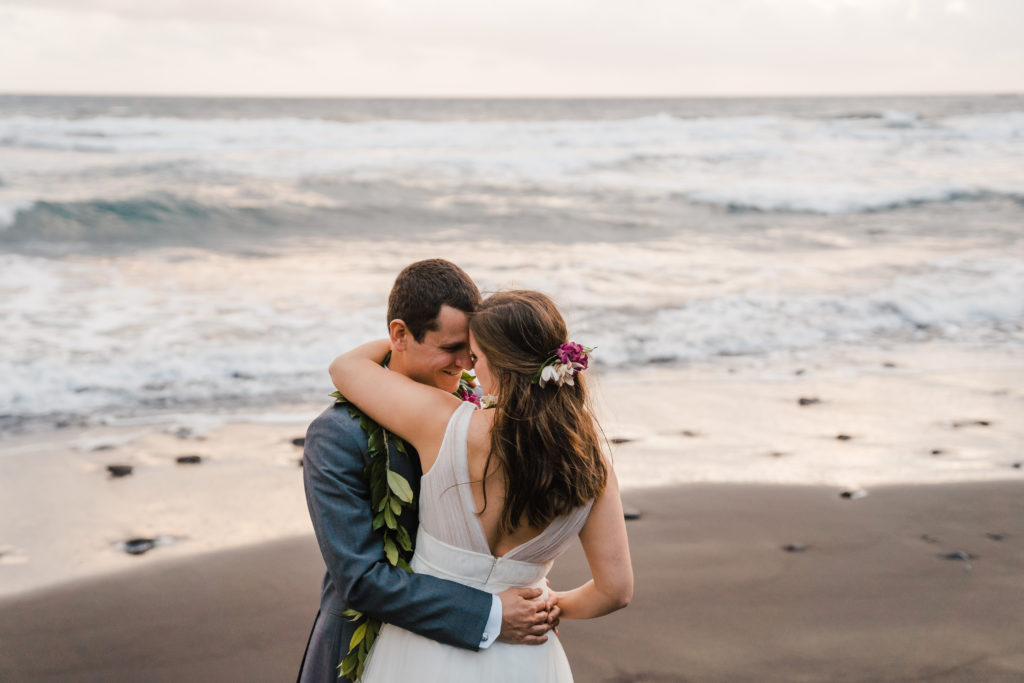 bride and groom dancing on black sand beach in hawaii